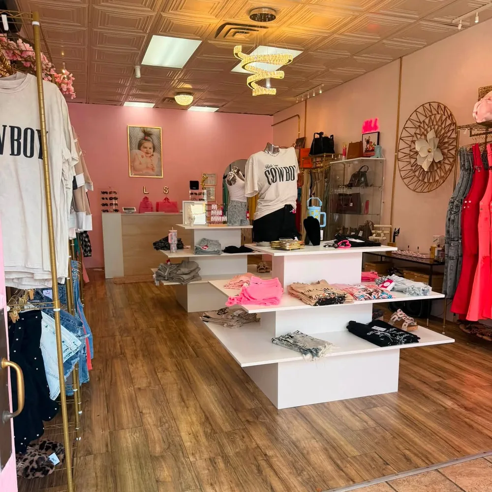 Inside the shop: gold spiral chandeliers, brass rails, white display tables of folded tees and a blush pink back wall.
